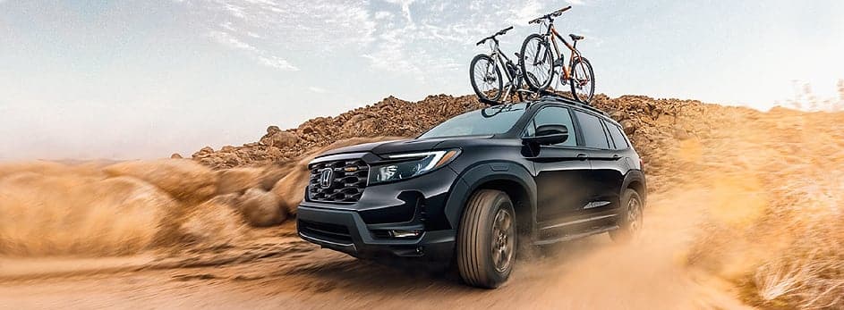 Black SUV with two bicycles on roof driving through desert terrain.