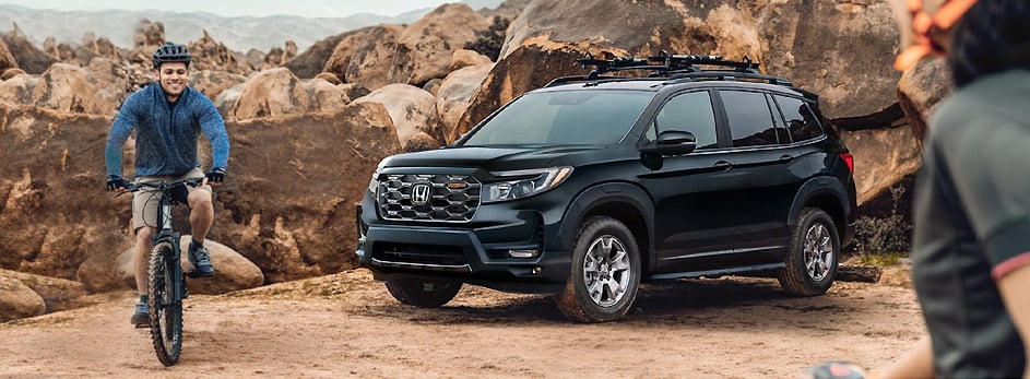 Man biking near a parked Honda SUV in a rocky outdoor setting.