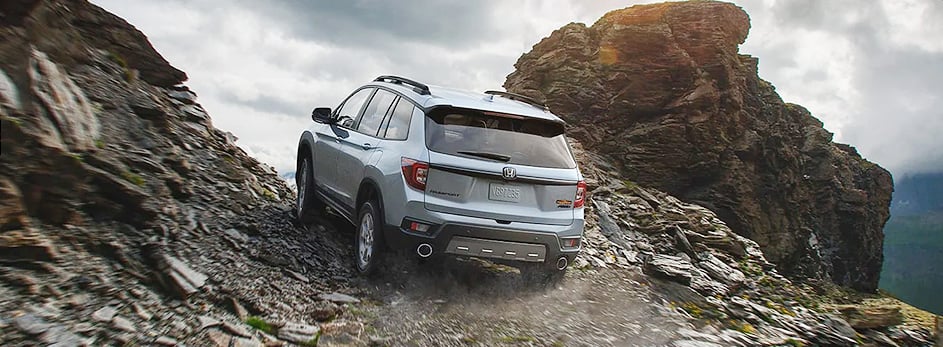 SUV driving on a rocky mountain trail under cloudy skies, showcasing off-road capability.