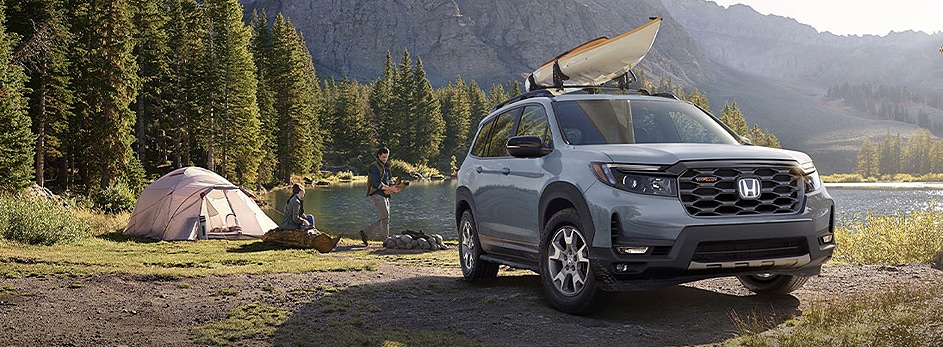 Honda SUV parked near a campsite by a lake, with a kayak on the roof and trees in the background.