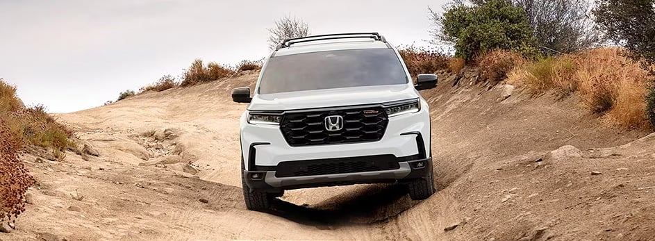 White Honda SUV on a rugged off-road trail, surrounded by dry shrubs and uneven terrain.