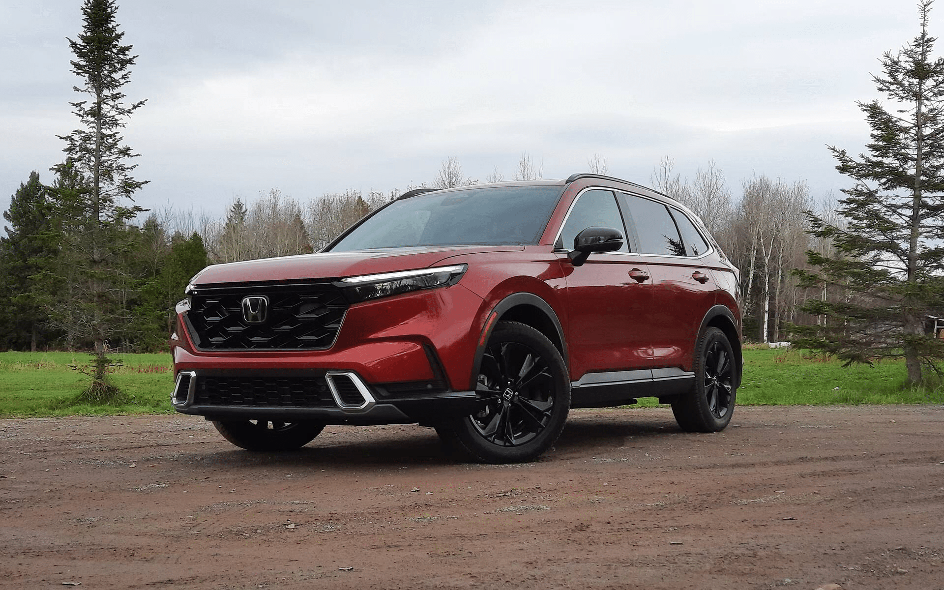 Red SUV parked on a dirt road with a forest background, highlighting its sleek design.
