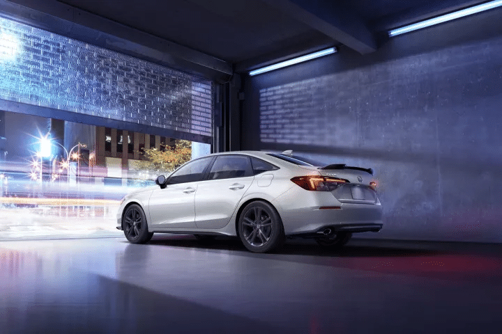 White sedan exiting a modern garage at night, with urban lights and motion blur in the background.