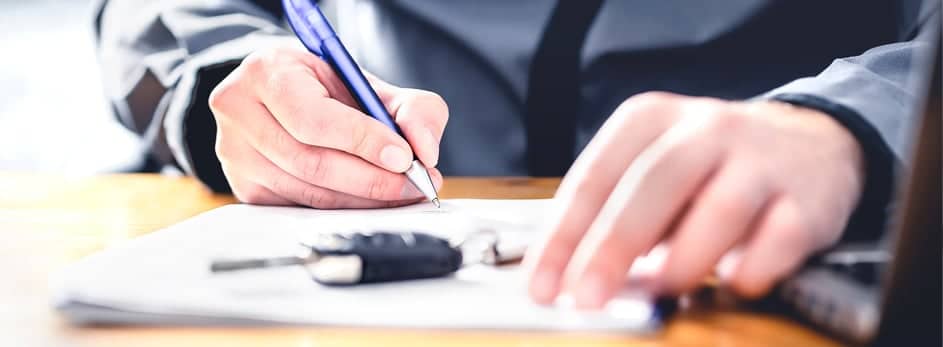 Person writing on paper with a blue pen, keys on the table nearby.