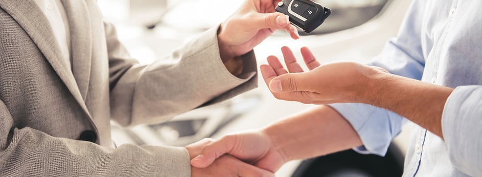 Person handing over car keys while shaking hands, symbolizing a car purchase or deal.
