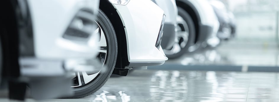 Row of white cars parked indoors on a glossy floor, showcasing their front ends and tires.