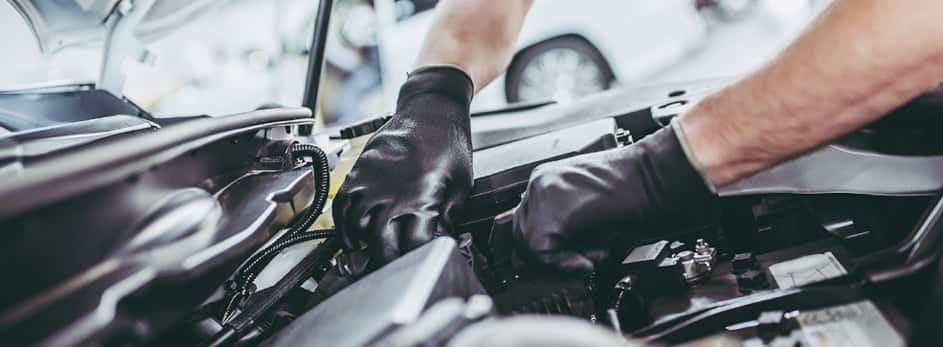 Mechanic wearing gloves works on car engine, performing maintenance or repairs. Auto service concept.