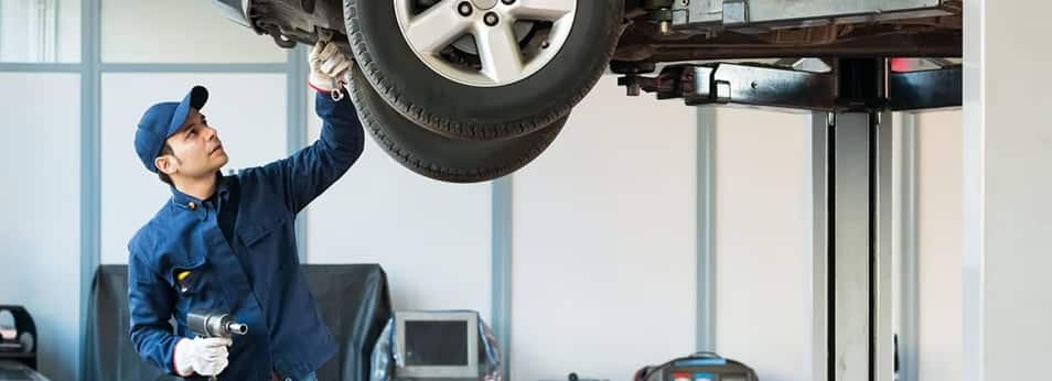 Mechanic inspecting a car on a lift in an auto repair shop, holding a flashlight.
