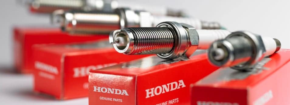 Close-up of Honda genuine spark plugs resting on branded red boxes.