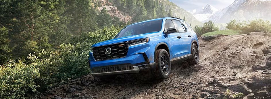 Blue SUV driving on a rugged mountain trail surrounded by dense green forest.