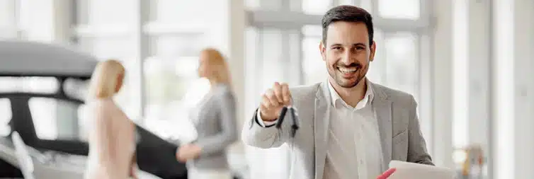 Smiling salesman handing over car keys in a dealership showroom.
